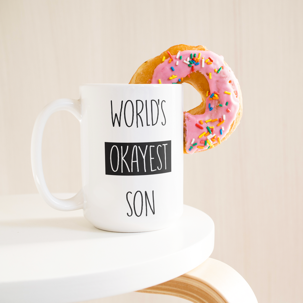 Okayest_son_15ozWhiteMugLifetsyleDonutLH_Mockup.png_15683847