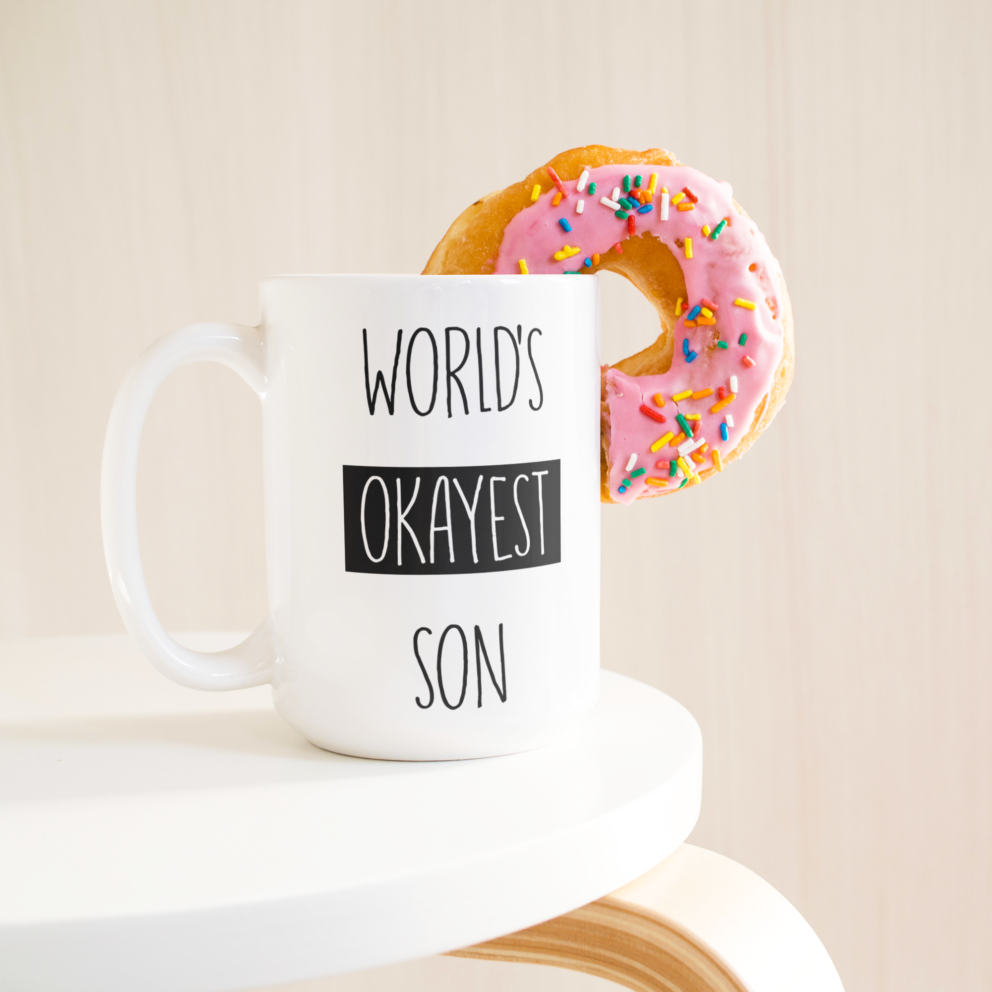Okayest_son_15ozWhiteMugLifetsyleDonutLH_Mockup.png_15683847